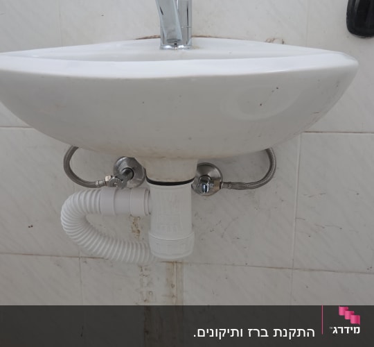 כיור עם ברז וצנרת מתחתיו על קיר לבן